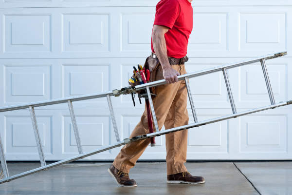 Handyman holding a ladder walking across a driveway